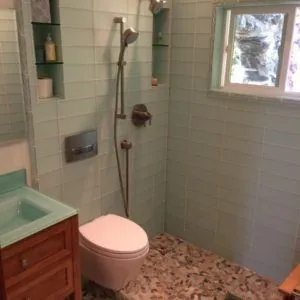 Curbless shower with seafoam glass subway tile, a pebble floor and tiled niches