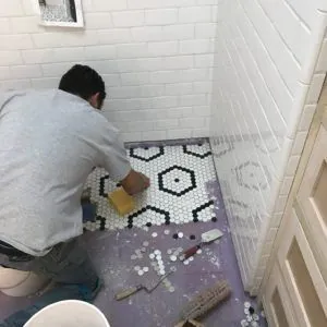 Tile setter installing a black and white hexagon mosaic floor in a white subway-tile shower
