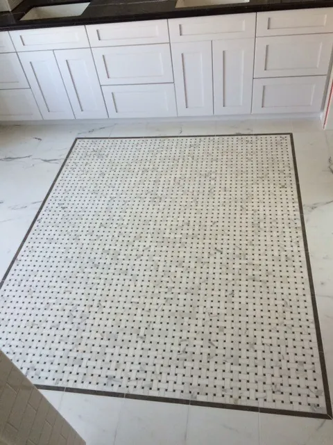 Bathroom floor with a white marble basketweave mosaic inset framed by a dark border