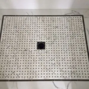 Shower floor of marble basketweave mosaic with a dark border and a square drain