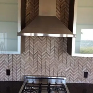 Chevron marble backsplash behind a stainless range hood and gas cooktop