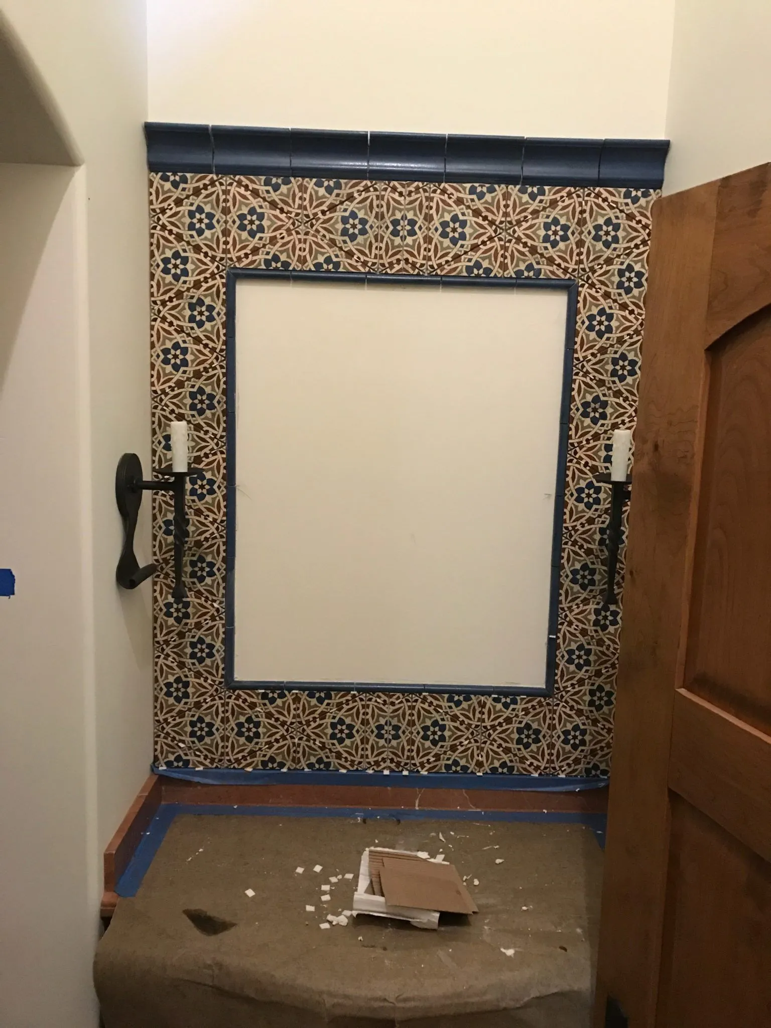 Blue and white Spanish-style tile surround framing a mirror niche beside a carved wood door