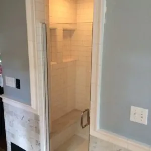 Shower with white tile walls, built-in niches and a tiled bench behind a glass door