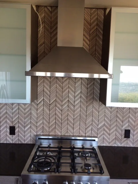 Chevron marble backsplash behind a stainless range hood and gas cooktop