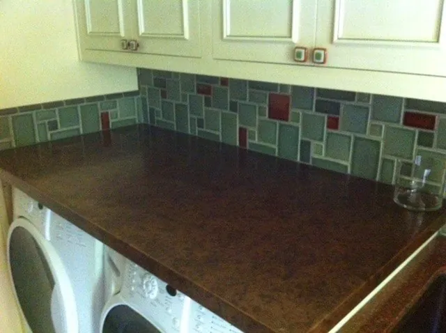 Laundry room backsplash of blue-green and red glass tile above a dark granite counter