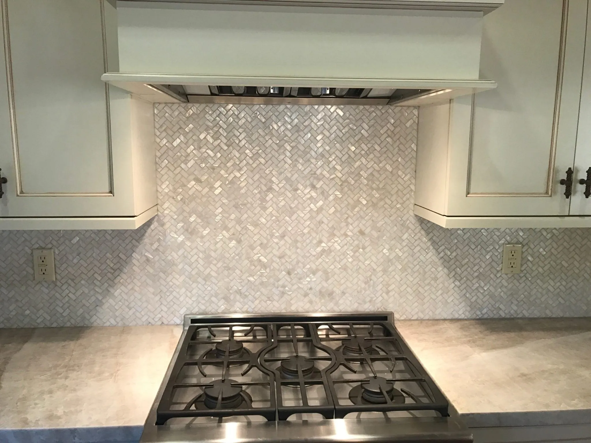 White marble herringbone kitchen backsplash behind a stainless steel gas range