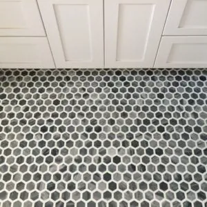 Gray and white hexagon mosaic bathroom floor in front of white cabinets