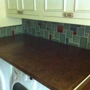 Laundry room backsplash of blue-green and red glass tile above a dark granite counter