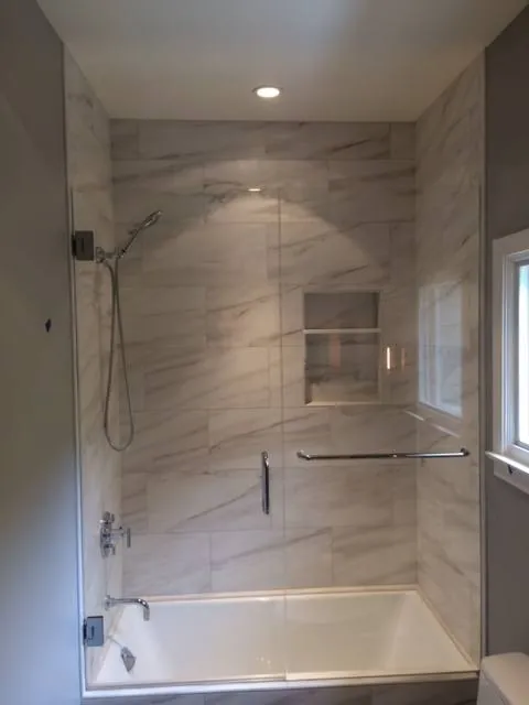 Tub-shower with large white marble-look wall tile, a recessed niche and a frameless glass door