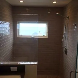 Walk-in shower in gray glass subway tile with an ocean-view window and a glass panel