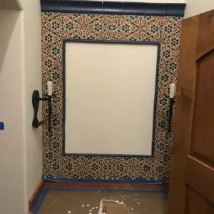 Blue and white Spanish-style tile surround framing a mirror niche beside a carved wood door