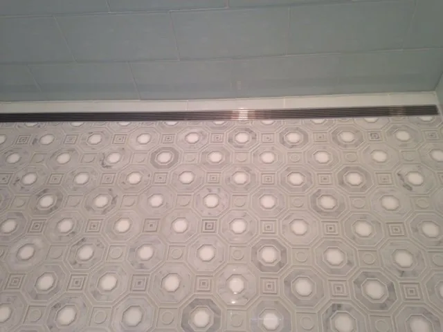 White and gray marble octagon-and-dot mosaic floor with a linear drain