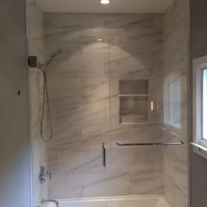 Tub-shower with large white marble-look wall tile, a recessed niche and a frameless glass door