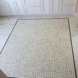 Bathroom floor with a white marble basketweave mosaic inset framed by a dark border
