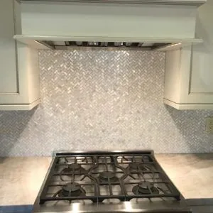 White marble herringbone kitchen backsplash behind a stainless steel gas range