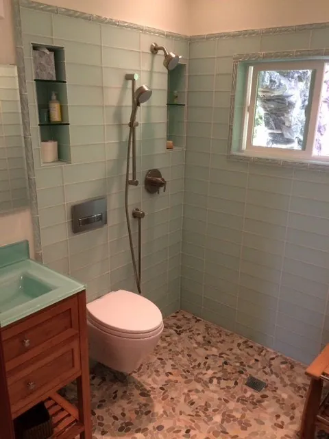 Curbless shower with seafoam glass subway tile, a pebble floor and tiled niches