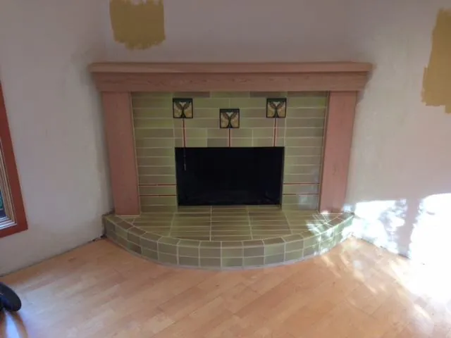 Corner fireplace in sage green craftsman tile with accent tiles and a curved hearth