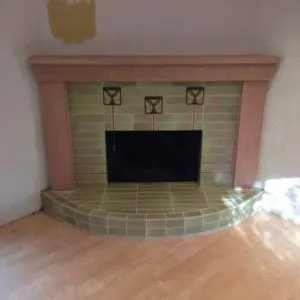Corner fireplace in sage green craftsman tile with accent tiles and a curved hearth